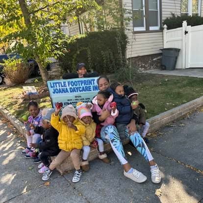 Caregiver and children sitting near the daycare sign